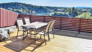 Una terraza de madera con una mesa y sillas, con vistas a un paisaje montañoso y una masa de agua.