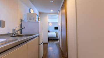 Un pasillo estrecho que conduce a un dormitorio con cama, una pequeña kitchenette con pileta y microondas, y piso de madera.