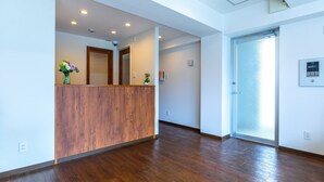 A reception area with a wooden reception desk, a glass door, and a wall-mounted control panel. - Mr.KINJO in front of Manza Beach (Onna)