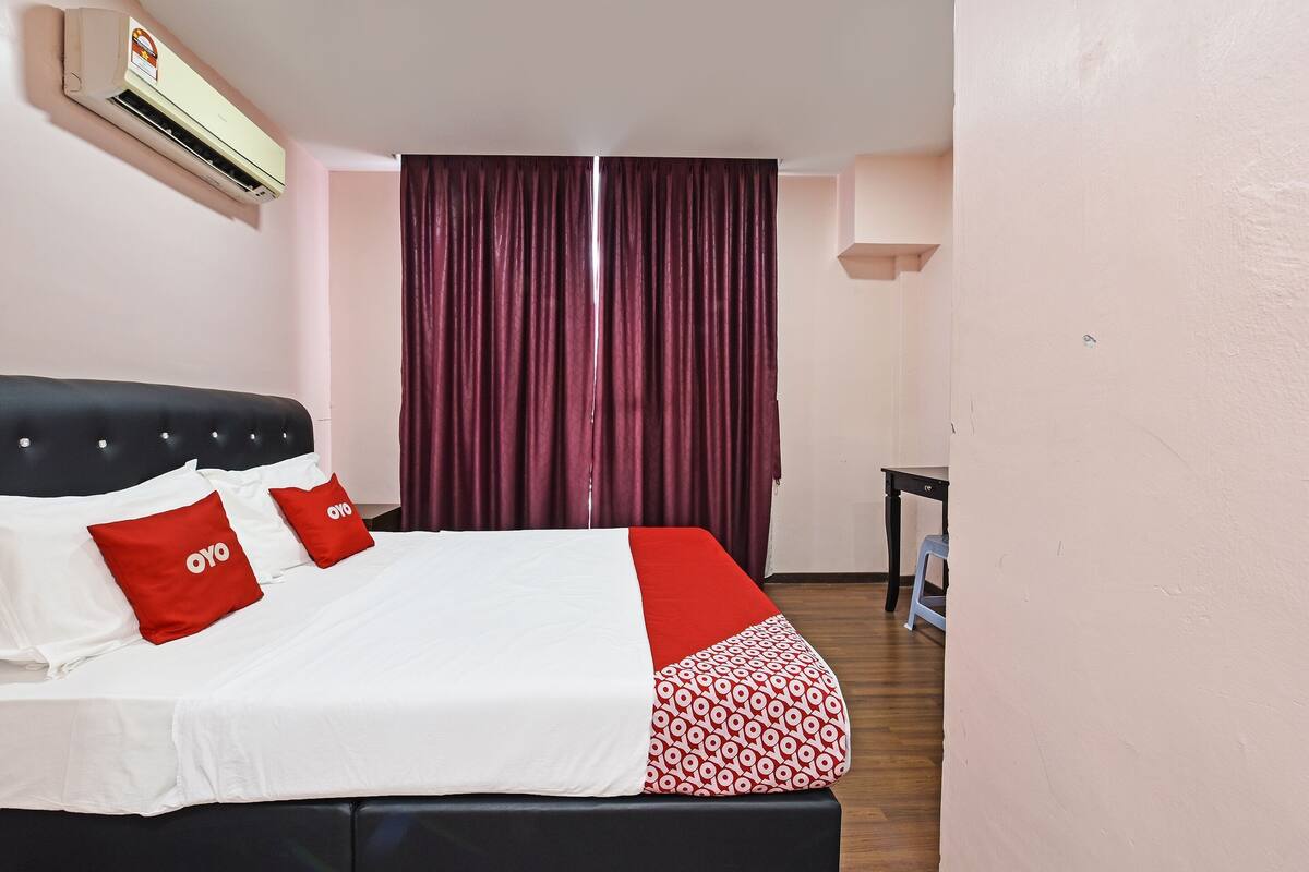 A neatly made bed with white and red bedding, a black headboard, and two red pillows with the logo "oyo".