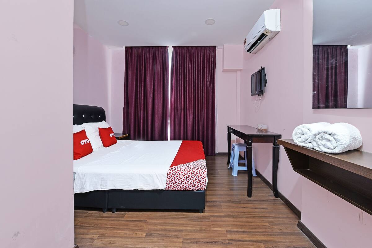 A hotel room with a bed, a desk, a mirror, and a window with curtains.