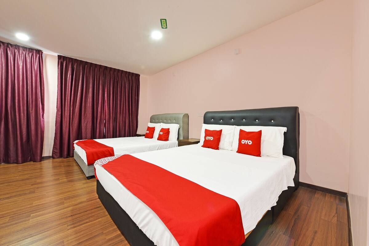 A hotel room with two beds, each with white bedding and red accents, and a wooden floor.