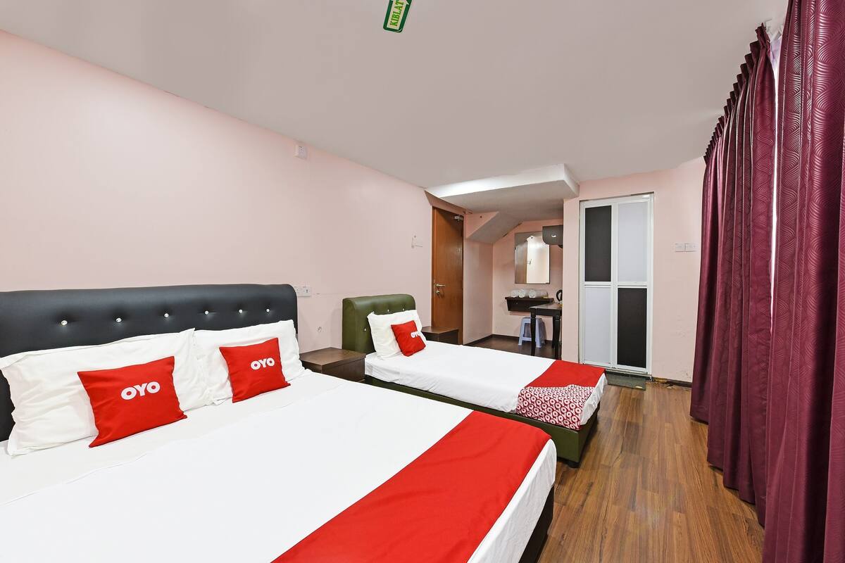 A hotel room with two beds, each with red and white bedding, a green chair, and a wooden floor.