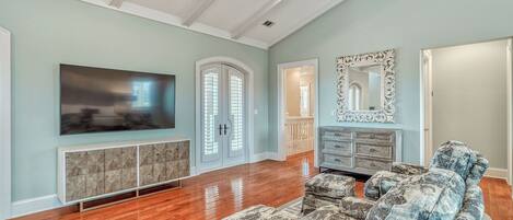 A spacious living room with hardwood flooring, a large flat-screen TV, a built-in entertainment unit, a patterned sofa, and a decorative mirror.