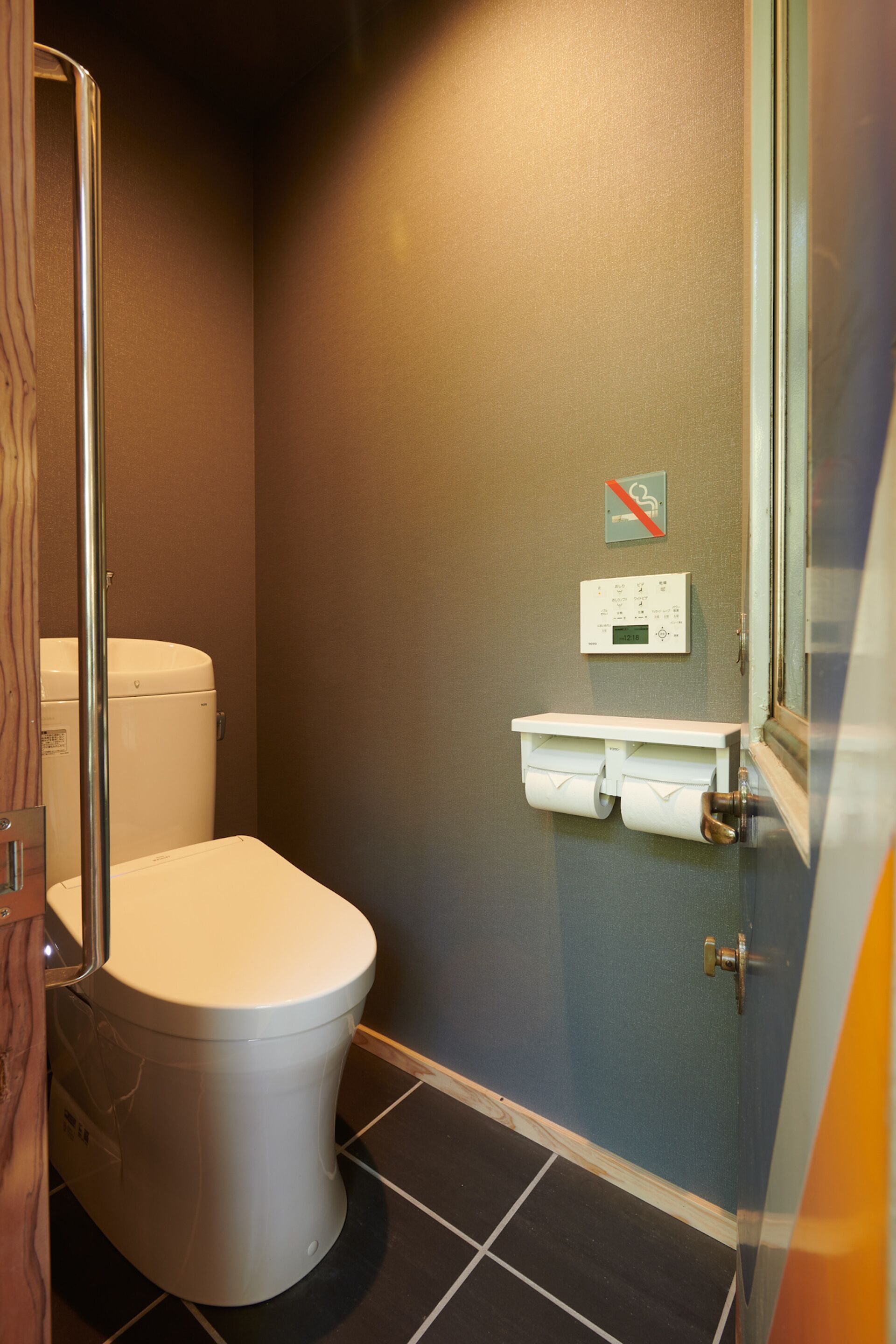 A small bathroom with a toilet, a wall-mounted toilet paper holder, and a hand dryer.