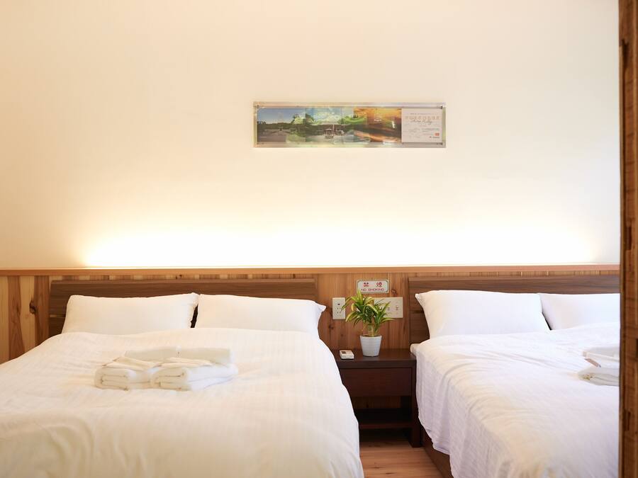 A hotel room with two beds, a wooden headboard, a nightstand with a plant, and a framed picture on the wall.