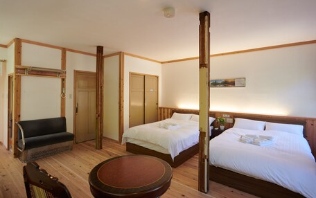 A hotel room with two beds, a wooden bench, a round table, and a small bedside table with a plant.