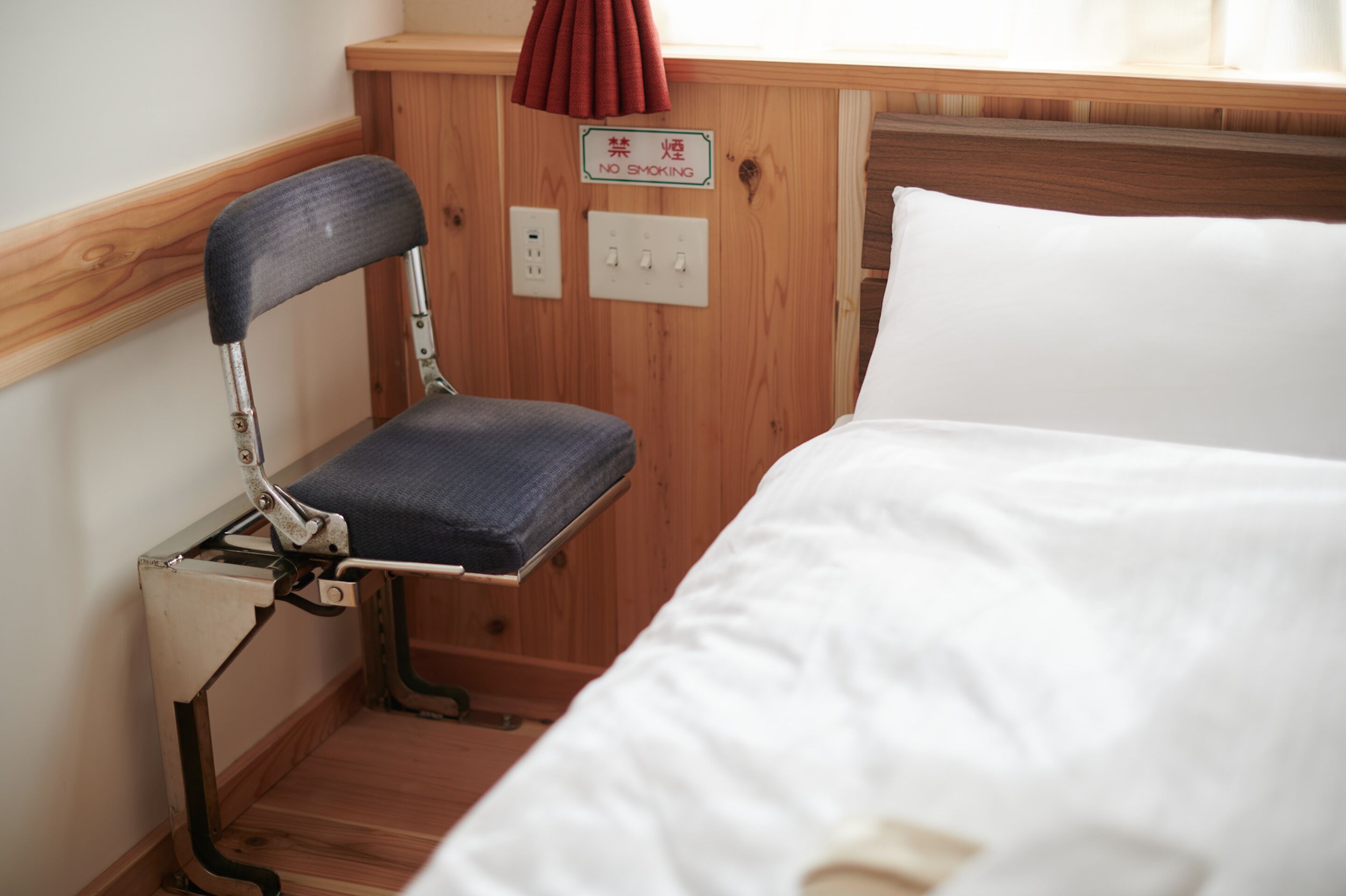 A wooden bunk bed with a white mattress and a metal chair with a blue cushion.