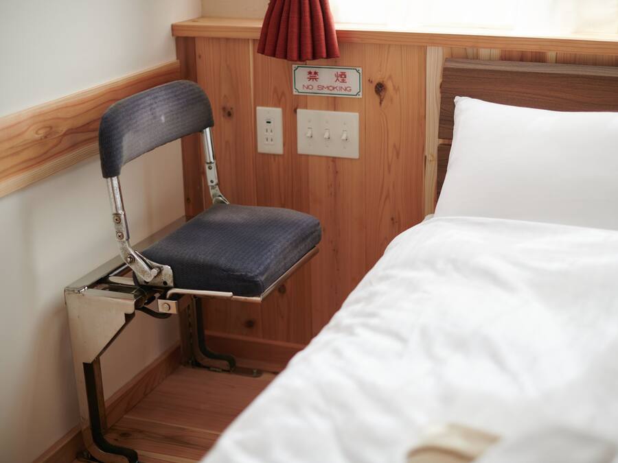 A wooden bunk bed with a white mattress and a metal chair with a blue cushion.