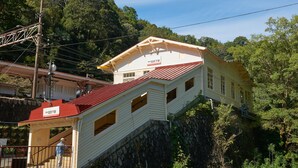 A two-story building with a red roof, situated on a rocky hillside surrounded by greenery. - The Railway Hotel Koyasan Pilgrimage Railway (Kudoyama)