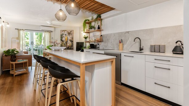 Una cocina moderna con una isla central, taburetes de bar y un comedor con vistas al exterior.