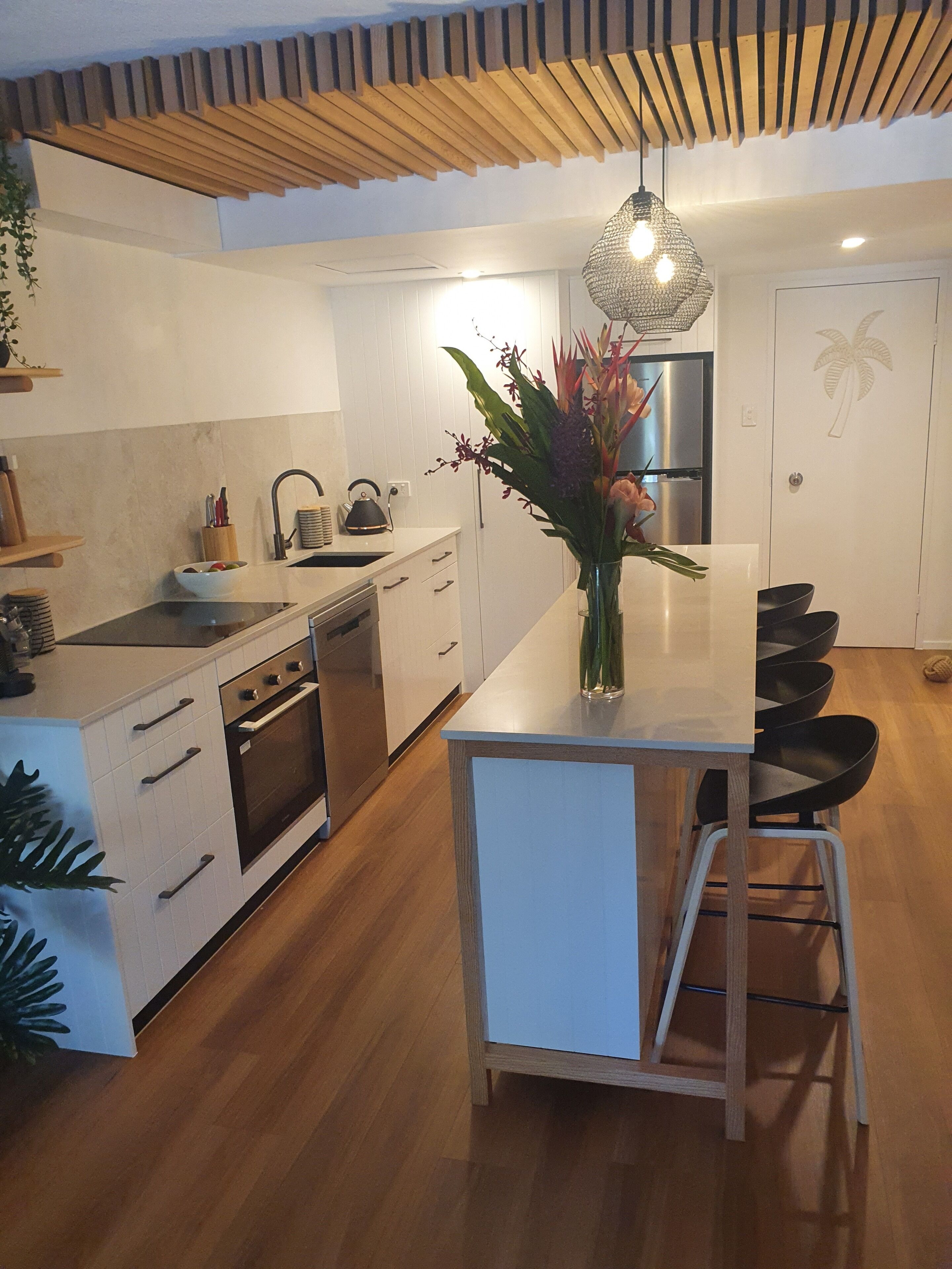 A modern kitchen with a central island, wooden ceiling, and a hanging light fixture.