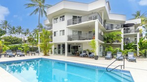 Un hotel moderno con piscina, varios balcones y jardines tropicales.