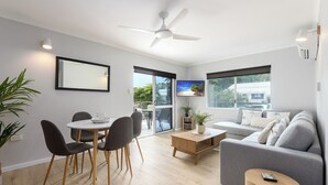 Una sala de estar moderna con un sofá gris, una mesa de comedor con sillas, una mesa de centro y un ventilador de techo.