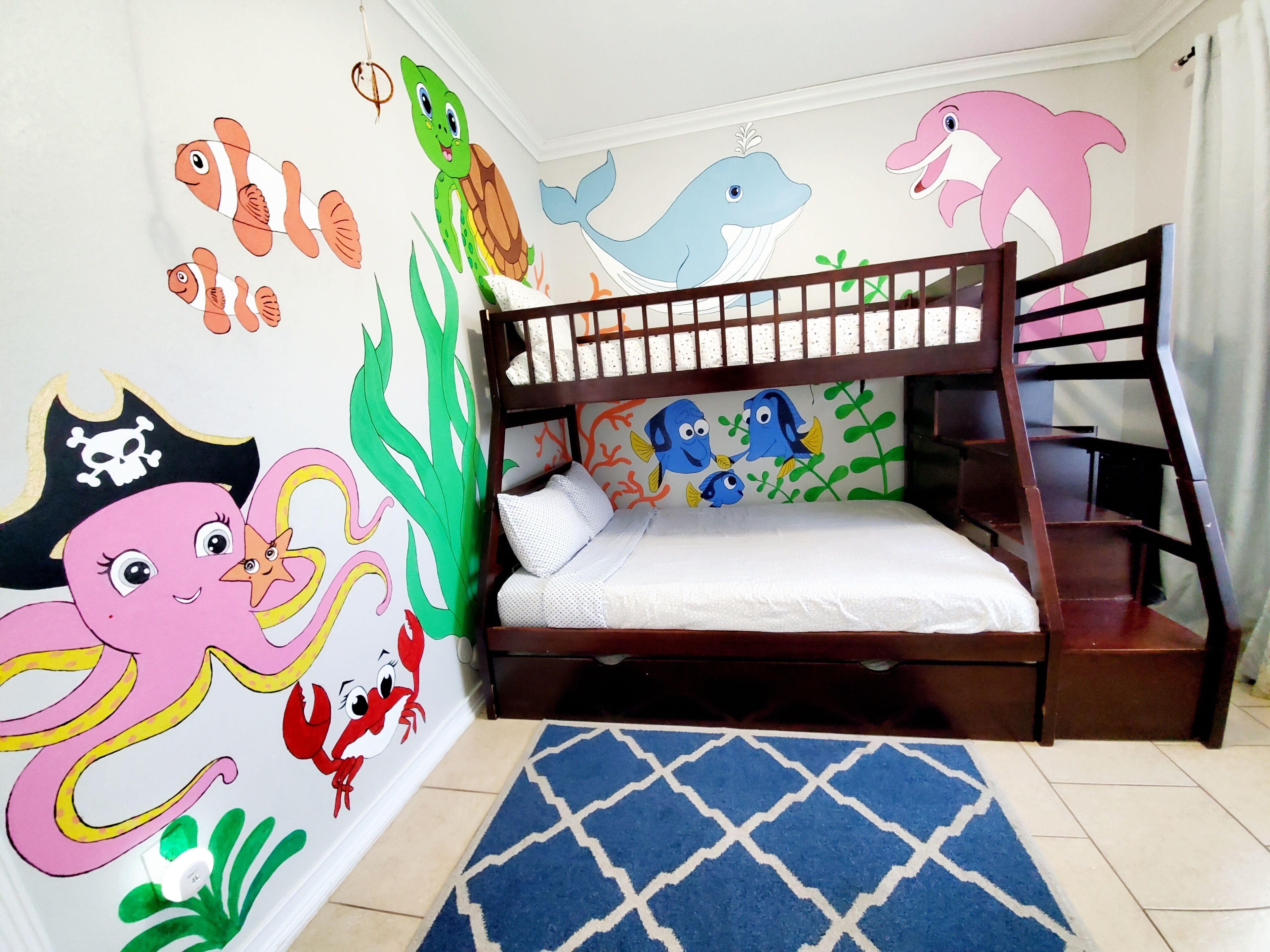 Een kinderkamer met een stapelbed, versierd met zeethemes decoratie, waaronder afbeeldingen van vissen, een schildpad en een walvis.