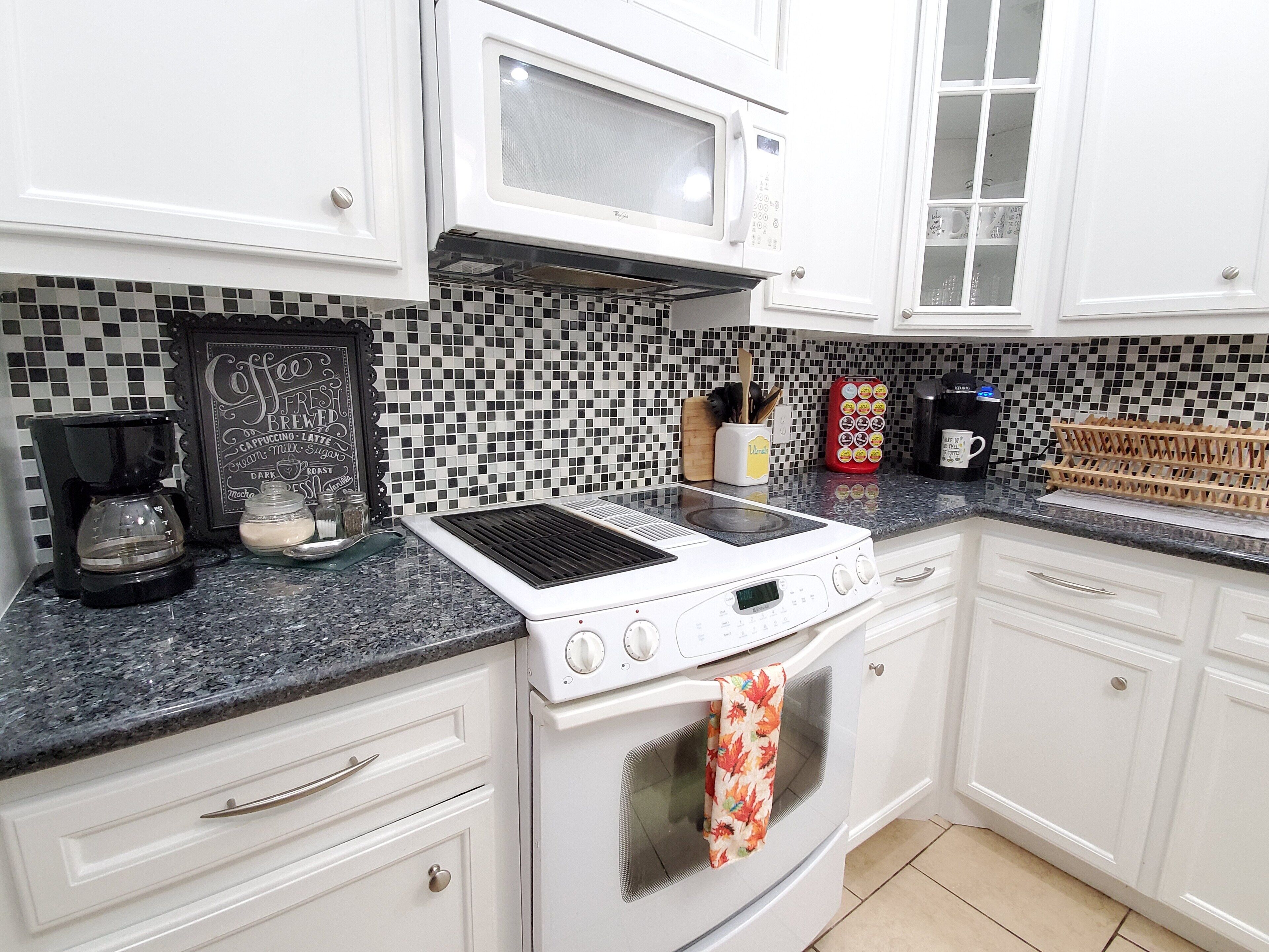 A kitchen with white cabinets, a microwave, a stove, and a coffee maker.