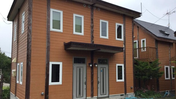 A two-story wooden house with a front porch, two doors, and a small garden area. - Ninjaart Furano Cottage (Furano)