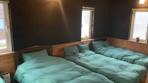 A room with two beds, dark walls, and a window with a curtain. - Ninjaart Furano Cottage (Furano)