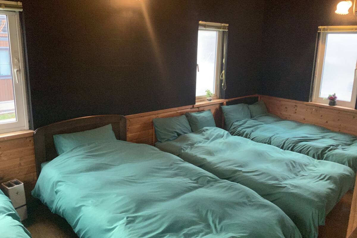 Une chambre avec deux lits, des murs sombres et une fenêtre avec un rideau.