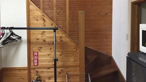A wooden staircase with a metal handrail, a clothes rack with hangers, and a red sign with Japanese characters. - Ninjaart Furano Cottage (Furano)
