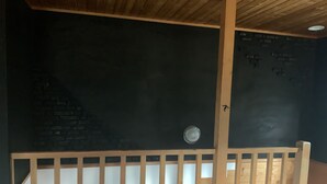 A room with a wooden ceiling, a brick wall, and a white crib. - Ninjaart Furano Cottage (Furano)