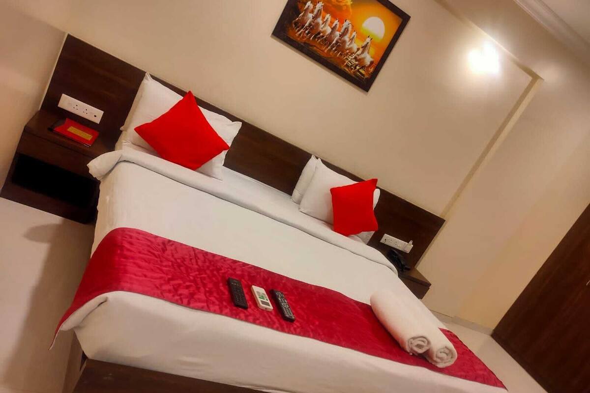 Une chambre d’hôtel avec un lit, une literie rouge et blanche, un tableau au mur et une table de chevet avec un téléphone et un livre rouge.