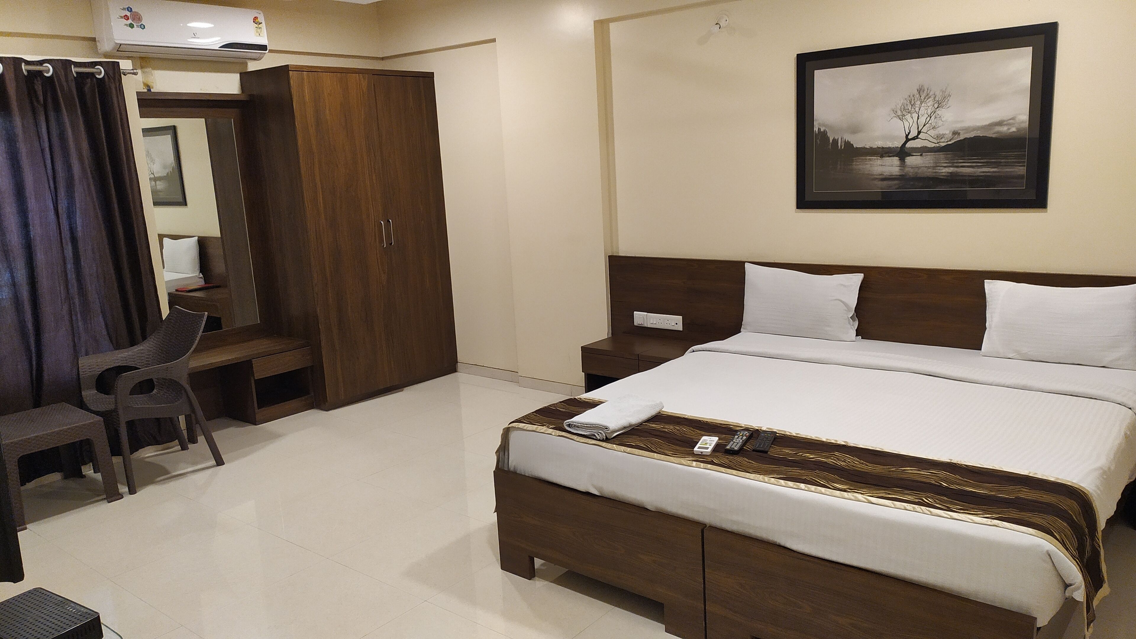 Une chambre d’hôtel comprenant un lit, une table de chevet, une chaise, une armoire et un tableau encadré au mur.
