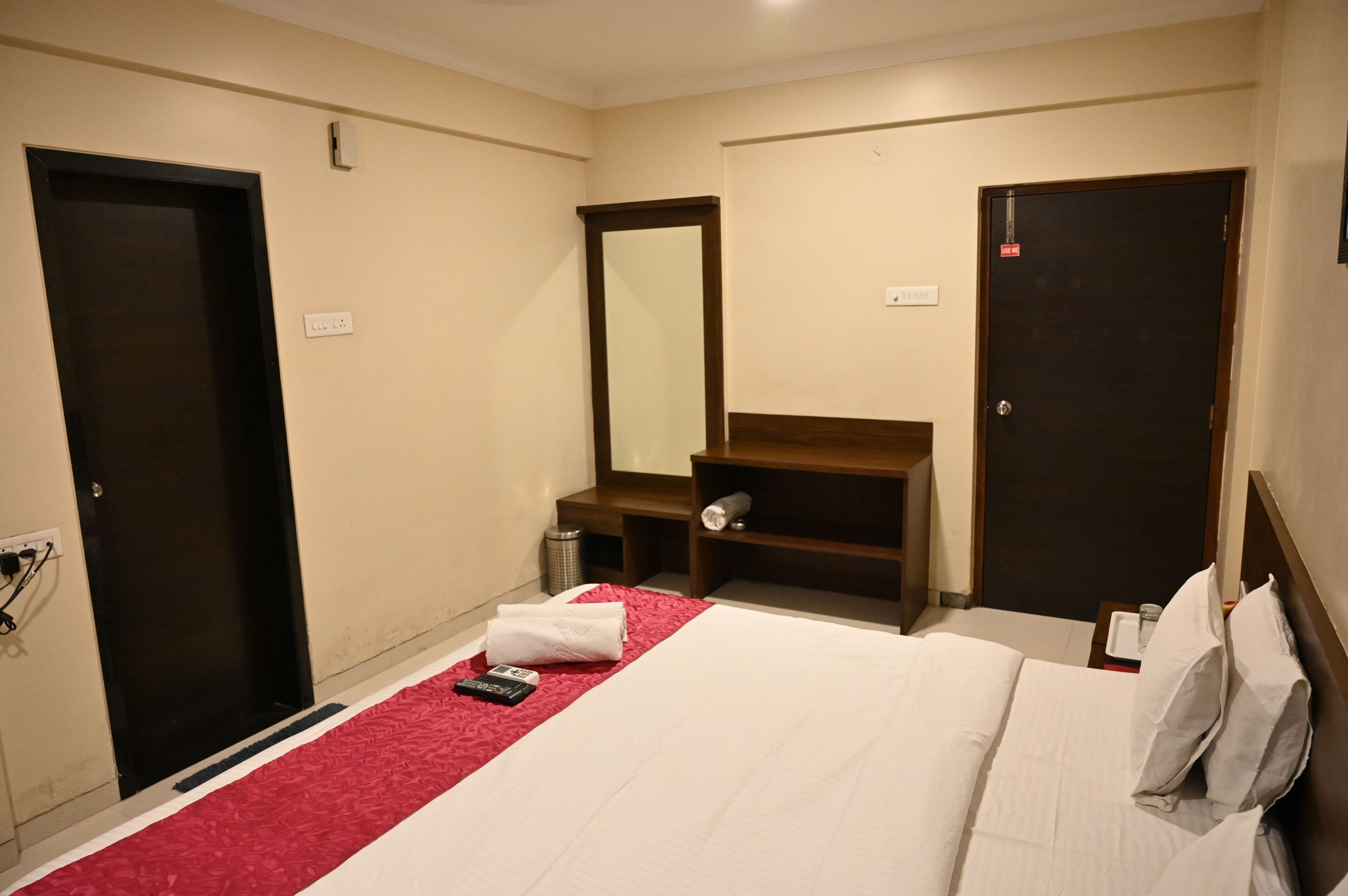 Une chambre d’hôtel avec un lit, un bureau, un miroir et deux portes.