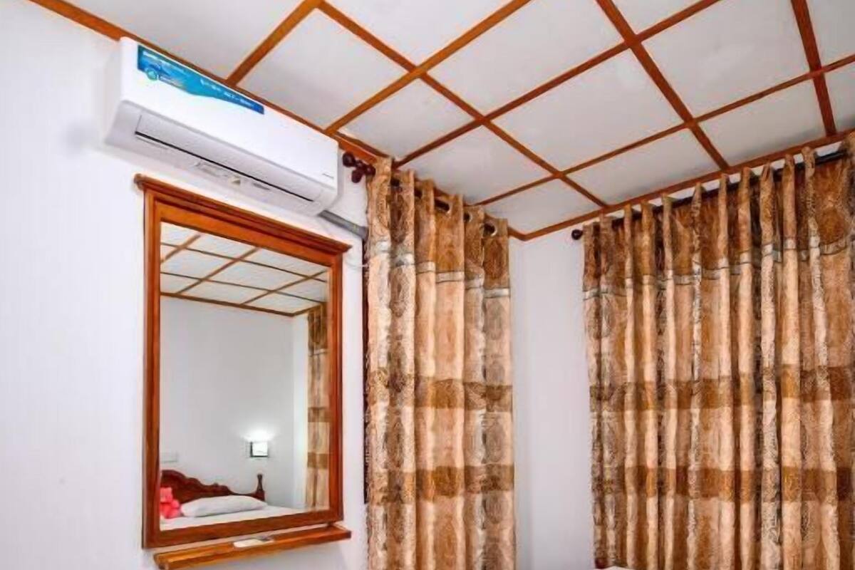 A bedroom with a wooden bed, a mirror, an air conditioning unit, and patterned curtains.