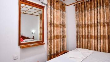 A bedroom with a wooden bed, a mirror, an air conditioning unit, and patterned curtains.
