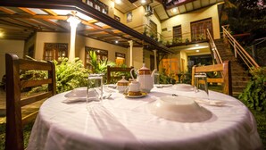 A well-lit outdoor dining area with a table set for tea service, surrounded by wooden chairs and a staircase leading to an upper level. - Wildlife Safari House (Udawalawa)
