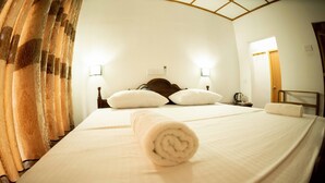 A neatly made bed with a rolled towel, two bedside lamps, and a wooden headboard in a hotel room. - Wildlife Safari House (Udawalawa)