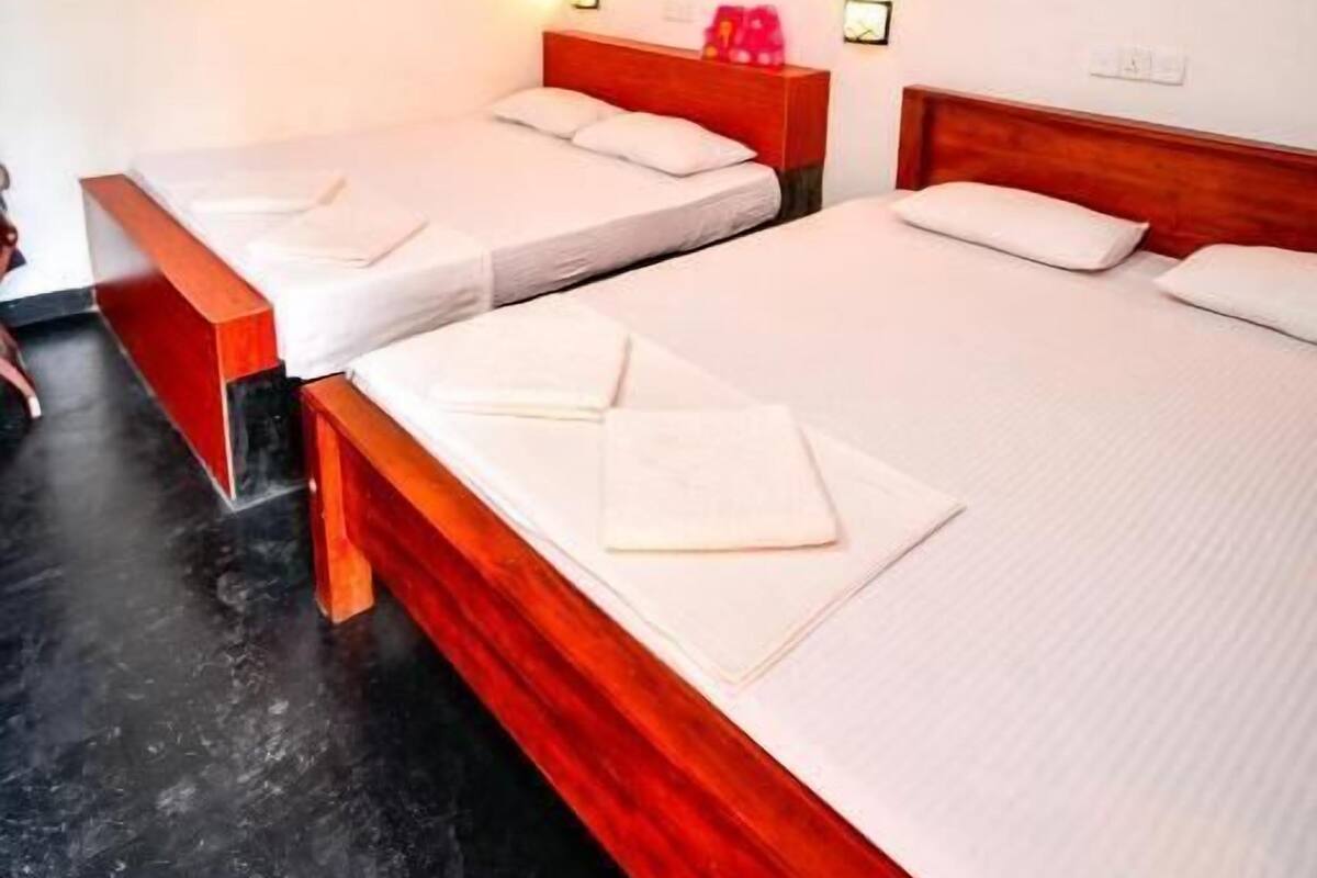 A hotel room with three single beds, wooden headboards, and bedside tables with lamps.