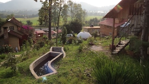 A rural setting with a house featuring a wooden staircase, a concrete water channel, and a large dome structure. - Viña Real Cabañas Rotamundos (Tacambaro)