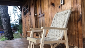 A wooden rocking chair with a woven seat and backrest, positioned on a wooden deck with a wooden wall in the background. - Viña Real Cabañas Rotamundos (Tacambaro)
