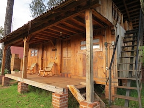 A rustic wooden cabin with a porch, two rocking chairs, and a ladder. - Viña Real Cabañas Rotamundos (Tacambaro)