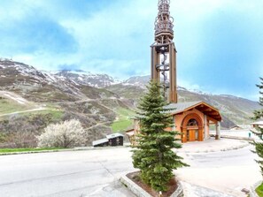 A mountain lodge with a bell tower, surrounded by snow-capped mountains and a clear sky.