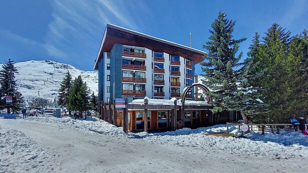 Un hôtel à plusieurs étages, avec un télésiège visible en arrière-plan, entouré de neige et d’arbres.