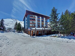 A multi-story hotel with a ski lift in the background, surrounded by snow and trees. - Chanteneige 403 by Interhome (Les Menuires)