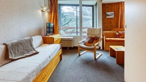 Une chambre d’hôtel confortable, avec un canapé, une chaise en bois, une petite table et une fenêtre avec des rideaux.