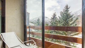 Un balcon avec une chaise blanche, une balustrade en bois et une vue sur des montagnes enneigées et des arbres à feuilles persistantes.