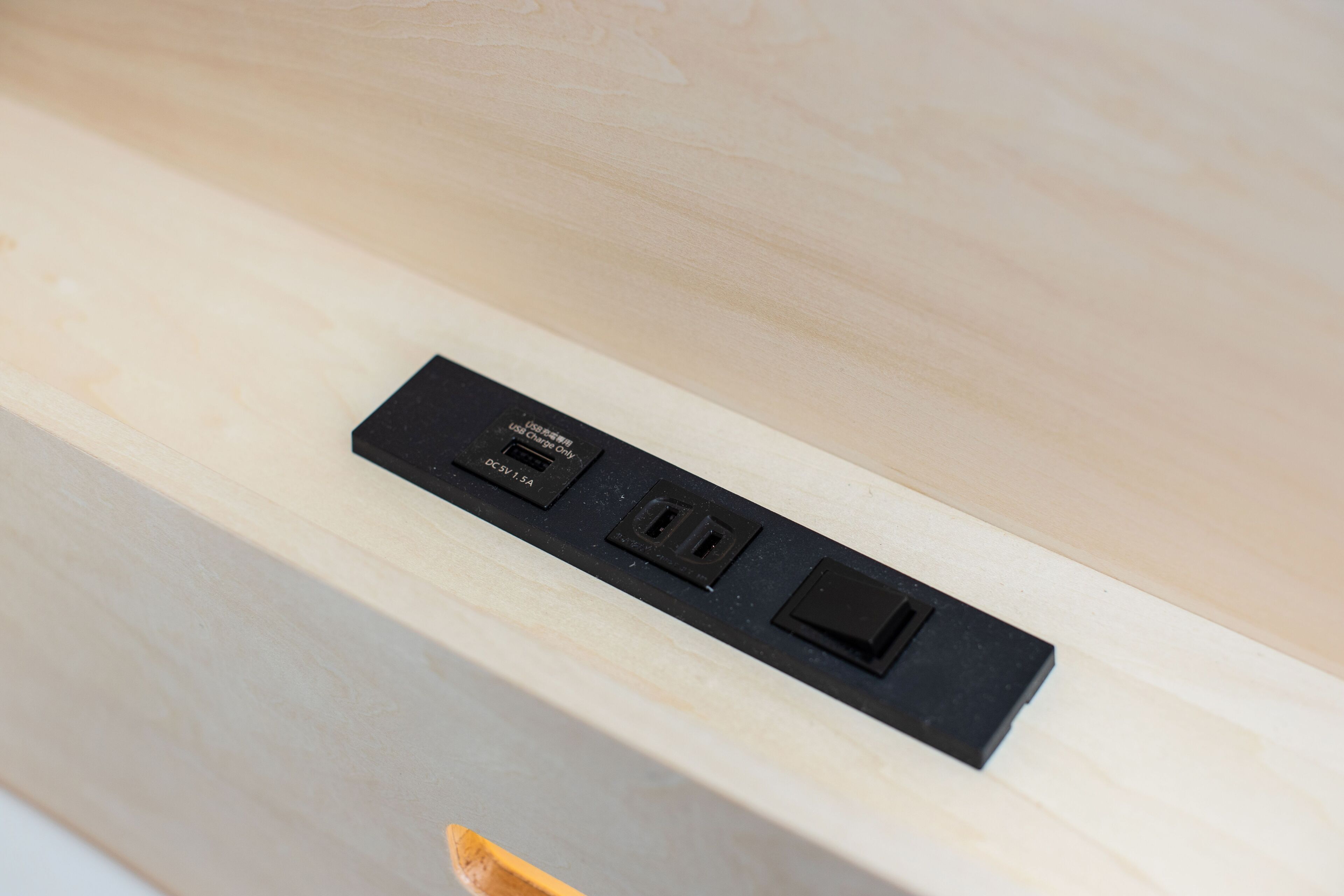 A black electrical outlet with three USB ports and a standard electrical outlet on a wooden surface.