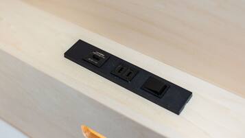 A black electrical outlet with three USB ports and a standard electrical outlet on a wooden surface.