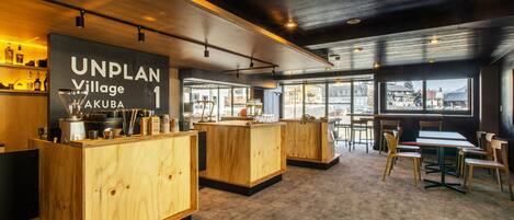 Un área de bar moderna con mostradores y asientos de madera, grandes ventanales con vistas a la ciudad, y un letrero visible que dice "UNPLAN Village 1".