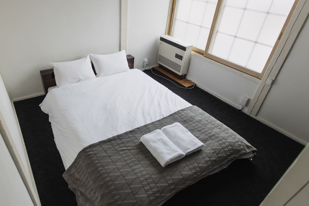 Ein ordentlich bezogenes Bett mit weißer und grauer Bettwäsche, ein kleiner Nachttisch und eine Heizung.