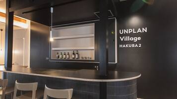 A modern bar area with a curved counter, a wine rack with bottles, and a sign reading "UNPLAN Village Hakuba 2".