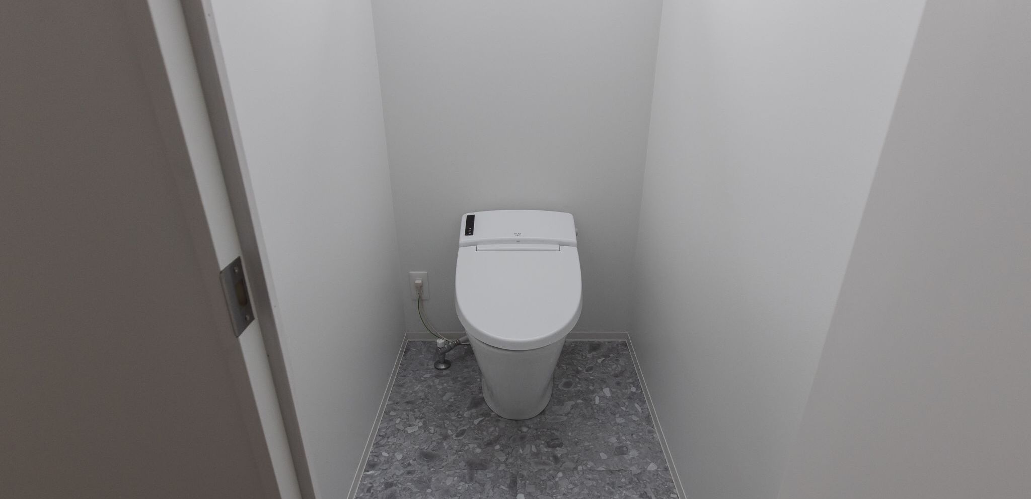 A small, modern bathroom with a toilet, a visible pipe, and a tiled floor.