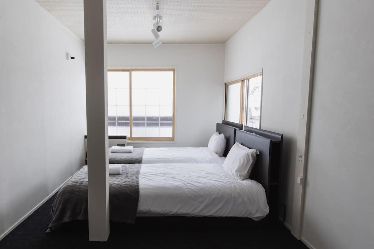 Ein schmales Hotelzimmer mit zwei Betten, einem großen Fenster und einem Deckenventilator.