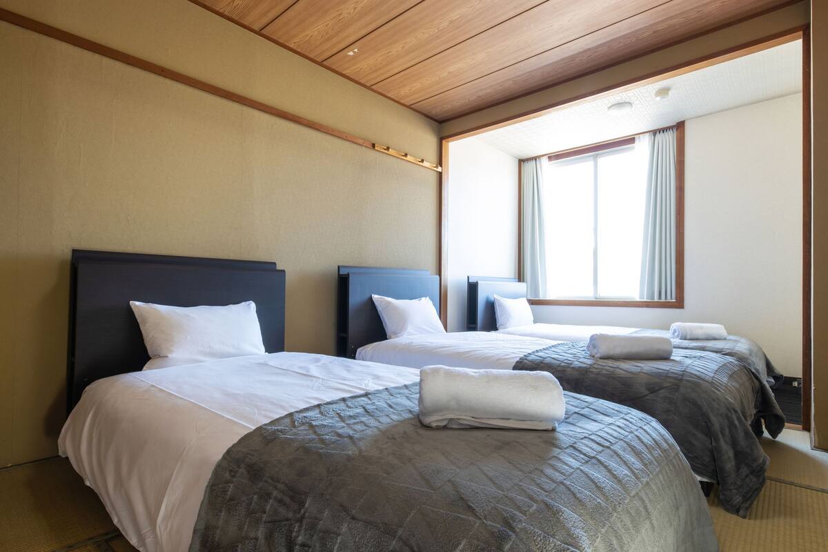 Ein Hotelzimmer mit zwei Betten, Holzboden und einem Fenster mit Vorhängen.