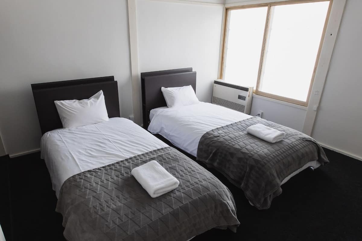 Ein Hotelzimmer mit zwei Einzelbetten, jeweils mit dunkelbrauner Kopfstütze und weißer Bettwäsche.